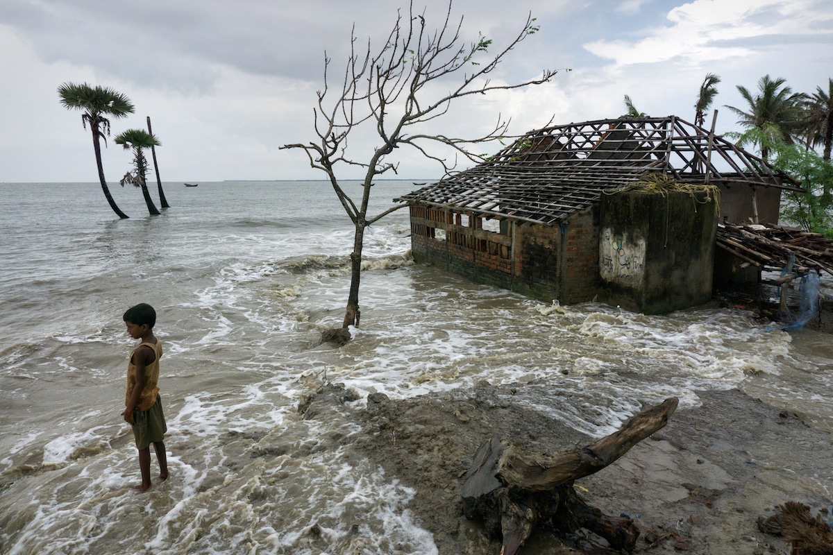 A boy stands near his flooded home which his family had to abandon due to sea level rise on Mousuni Island in West Bengal, India