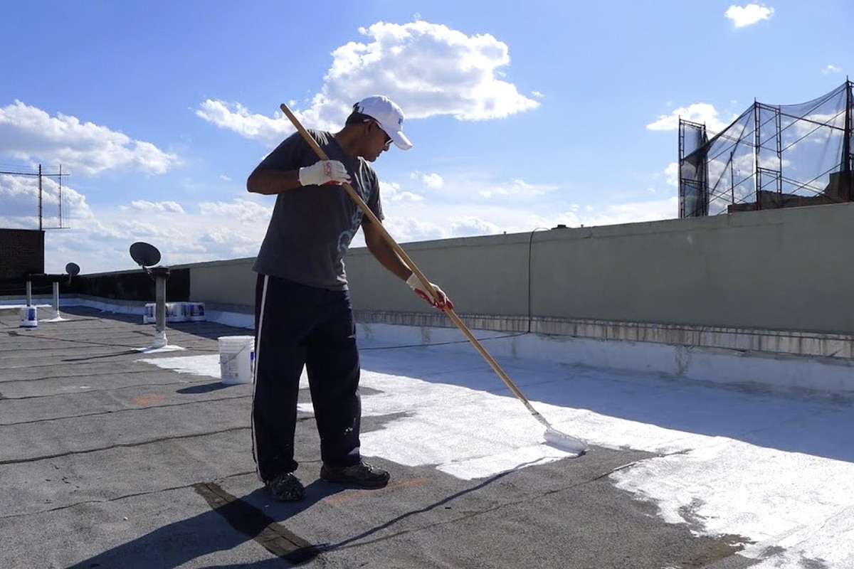A volunteer with the NYC CoolRoofs program paints a reflective coating on a building's rooftop to reduce heat absorption