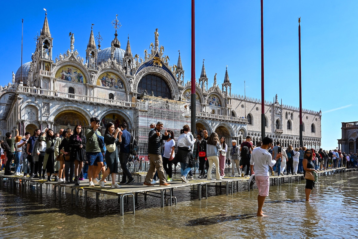 Tourists walk across elevated walkways outside St. Mark's Basilica on St. Mark's square in Venice, Italy following a high tide event