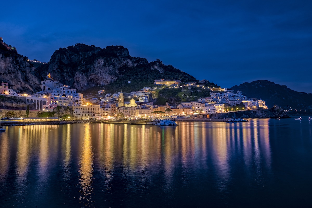 Illuminated houses at night in the town of Amalfi, Italy, reflecting in the Mediterranean Sea