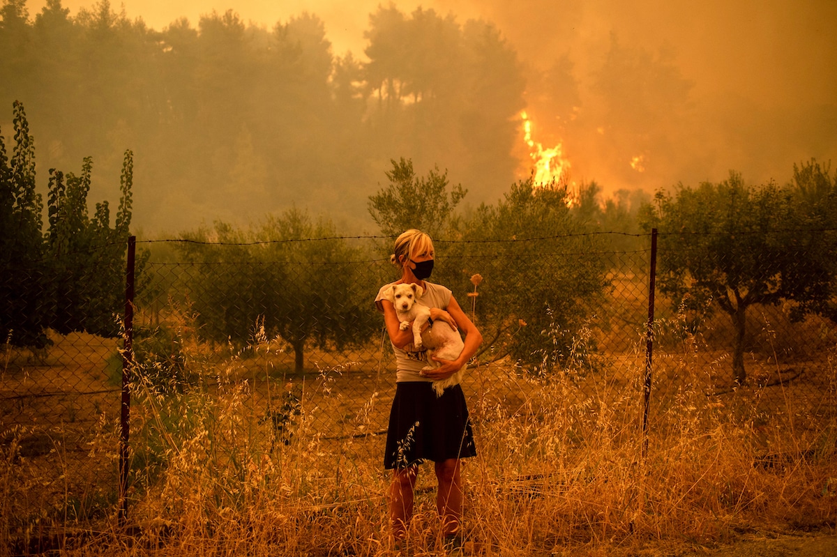 A woman holds a dog as forest fires approach the village of Pefki on Evia (Euboea) Island, Greece's second largest island