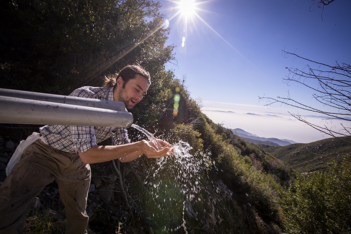 Activist Bridger Zadina drinks from spring water pouring from a pipe beside a water collection tunnel in the San Bernardino National Forest