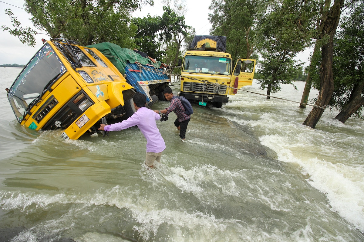 People wade past stranded trucks on a flooded street in Bangladesh, where floods are an increasing threat