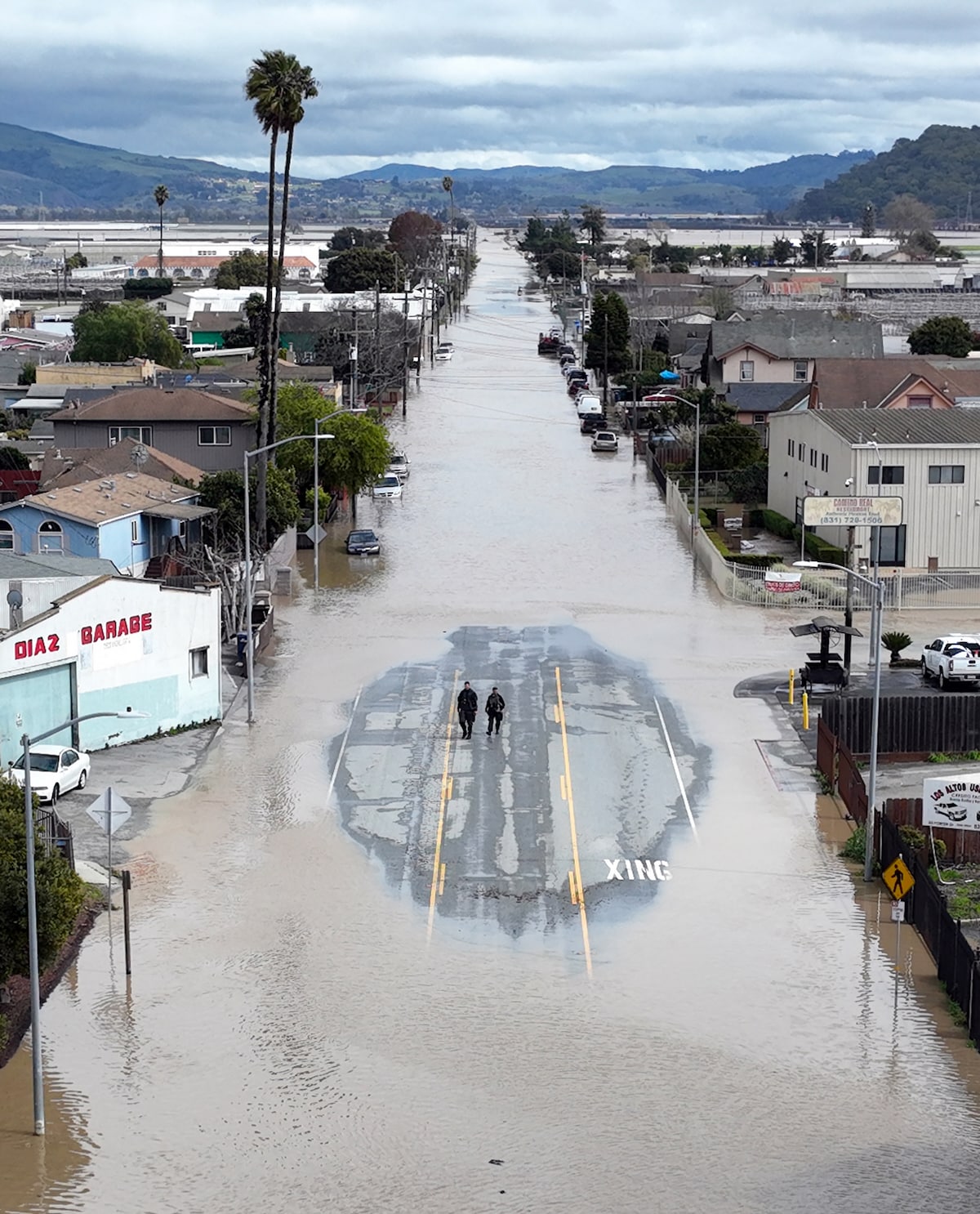 Aerial view of two people standing in a small patch of road amid floodwaters in Pajaro, California