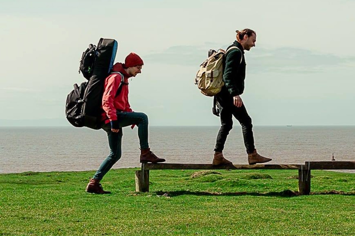 Filkin's Drift band members Seth Bye and Chris Roberts walking with their gear along the coast of Wales