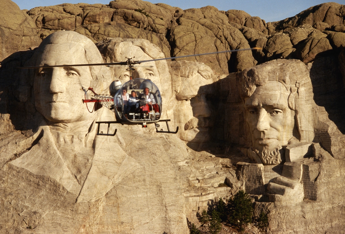 A tourist helicopter flies by Mount Rushmore National Monument