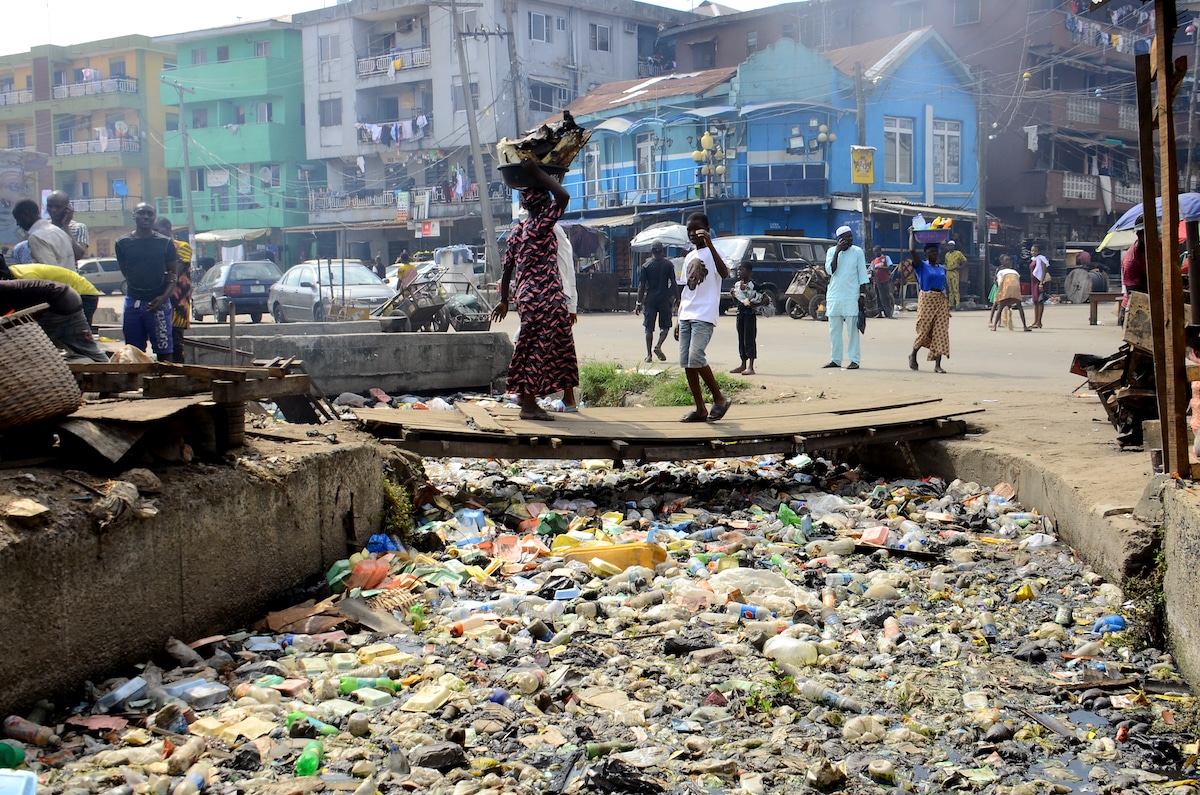 People walk past a drainage channel blocked with bottles and styrofoam food containers along Adeniji Adele on Lagos-Island in Lagos, Nigeria