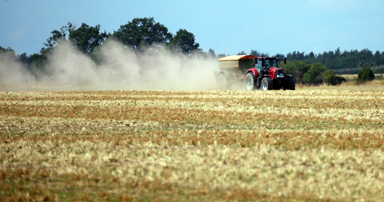 A farmer in a tractor spreads fertilizer on a grain field, leaving a large dust cloud behind near Berlin, Germany