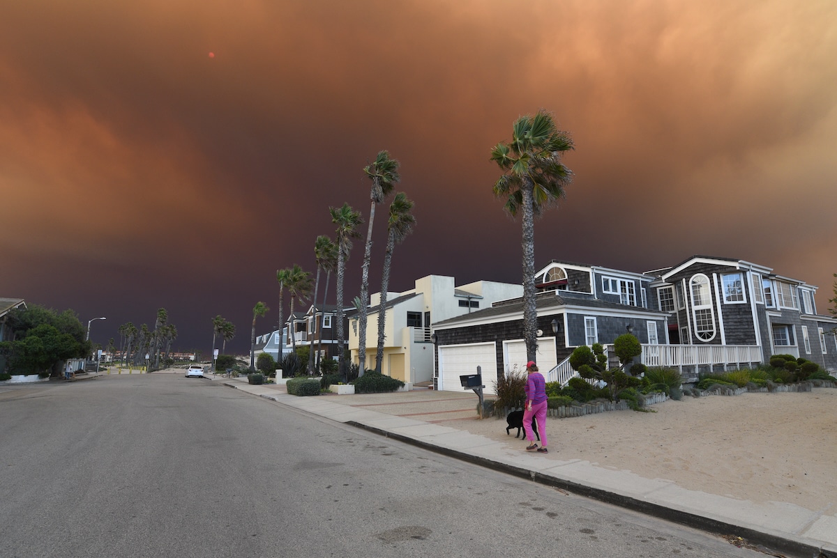 A resident walks her dog while smoke from wildfires darkens the afternoon skies at Oxnard Shores Beach, California