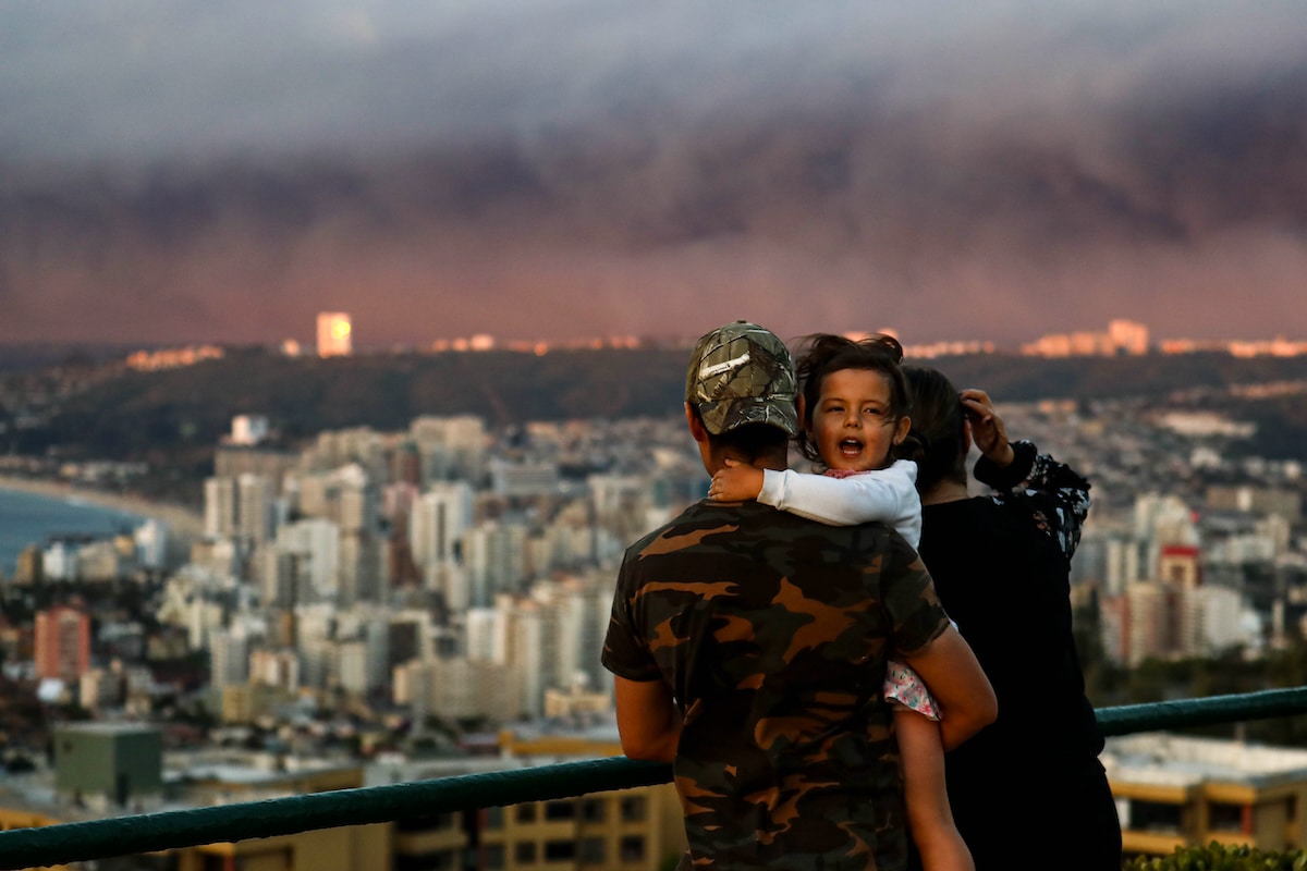 A girl hugs her father while overlooking wildfire smoke filling the sky in the distance in Valparaiso, Chile