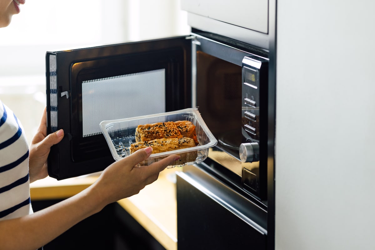 A person reheats a processed, packaged meal in a microwave oven