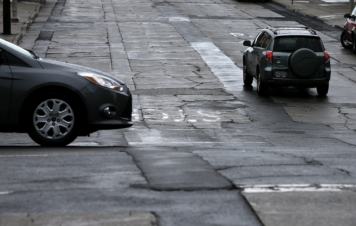 Cars drive on a street with cracked asphalt in San Francisco, California