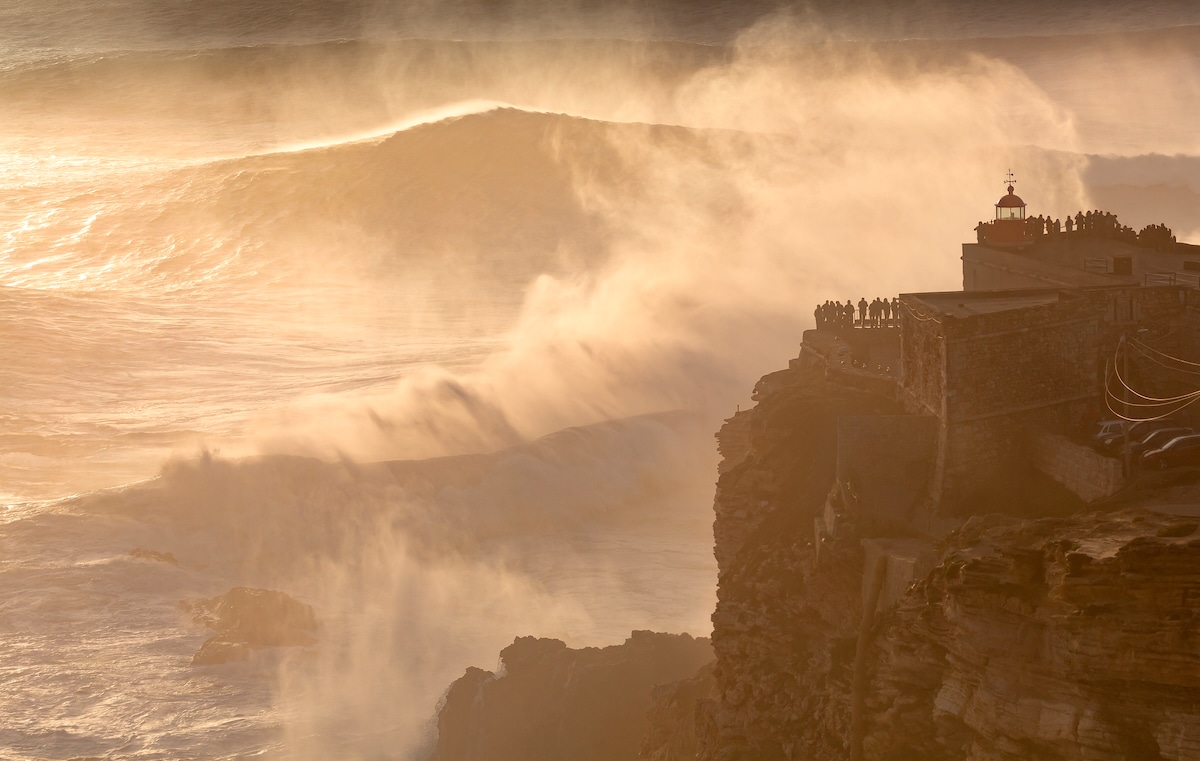 People watch from a cliff as Atlantic Ocean waves crash and release mist on the coast of Nazare, Portugal